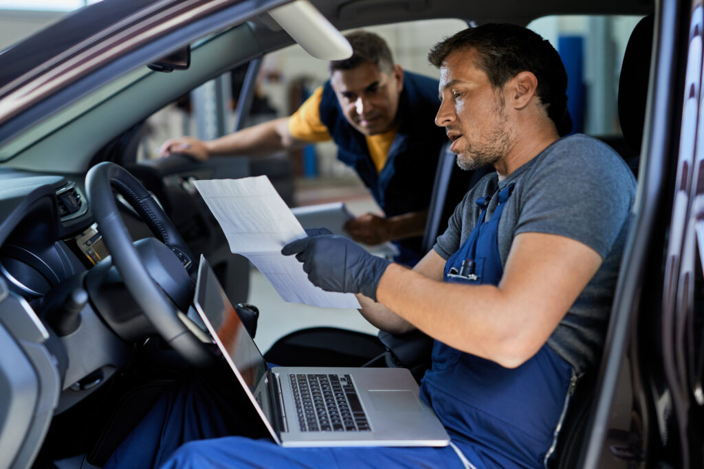 auto-repairman-talking-his-colleague-while-running-car-diagnostic-analyzing-data-workshop