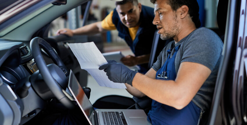 auto-repairman-talking-his-colleague-while-running-car-diagnostic-analyzing-data-workshop